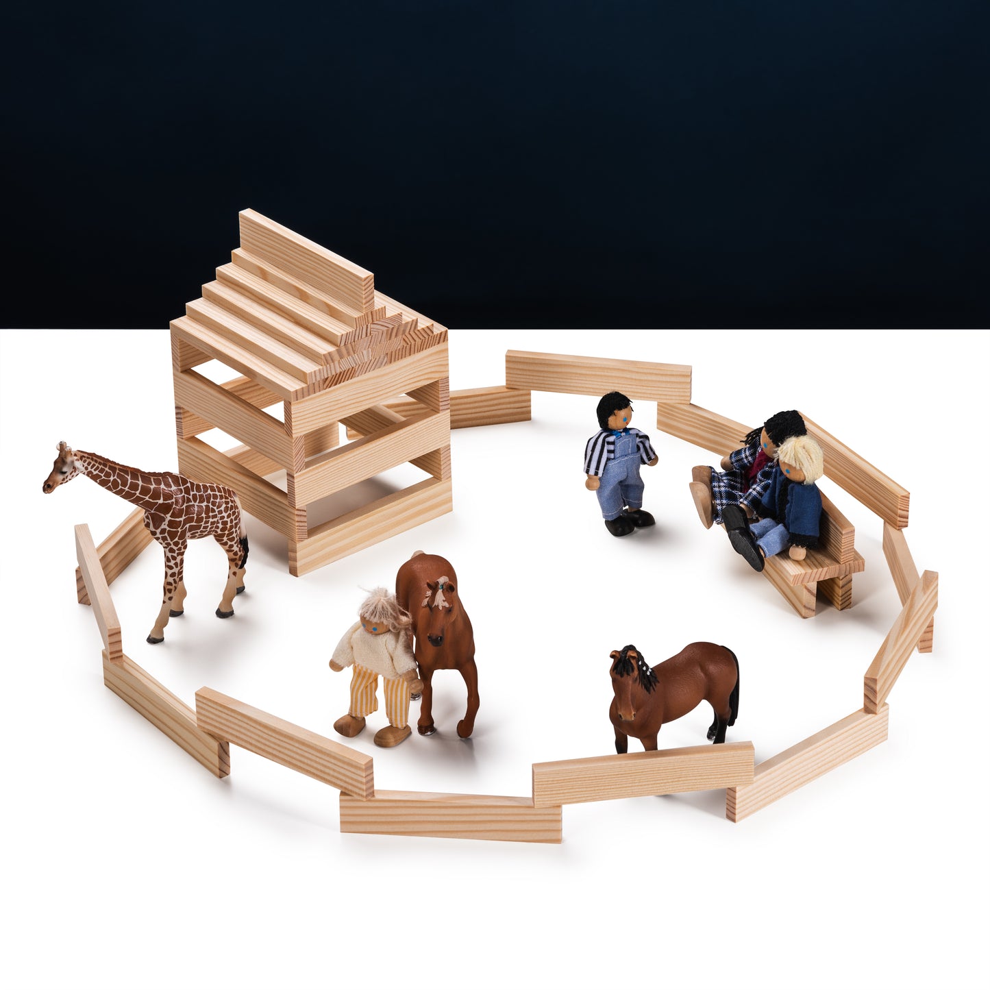 Holzklötze formen ein Gebäude und eine Einfriedung, umgeben von Spielzeugtieren und -figuren auf dunklem Hintergrund.