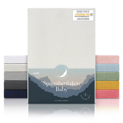 Verpackung von elfenbeinfarbenen Spannbettlaken für Babys mit Öko-Tex Standard 100 Siegel präsentiert neben einem Stapel Laken in verschiedenen Farben.