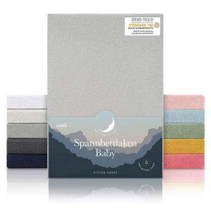 Verpackung von grauen Spannbettlaken für Babys mit Öko-Tex Standard 100 Siegel präsentiert neben einem Stapel Laken in verschiedenen Farben.