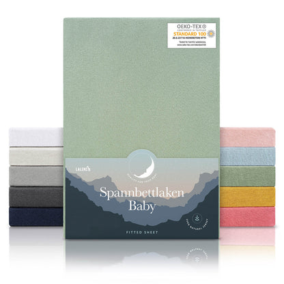 Verpackung von grünen Spannbettlaken für Babys mit Öko-Tex Standard 100 Siegel präsentiert neben einem Stapel Laken in verschiedenen Farben.