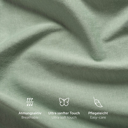Nahaufnahme der Textur eines grünen Spannbettlakens mit Symbolen für Atmungsaktivität ultra weichen Touch und Pflegeleichtigkeit.