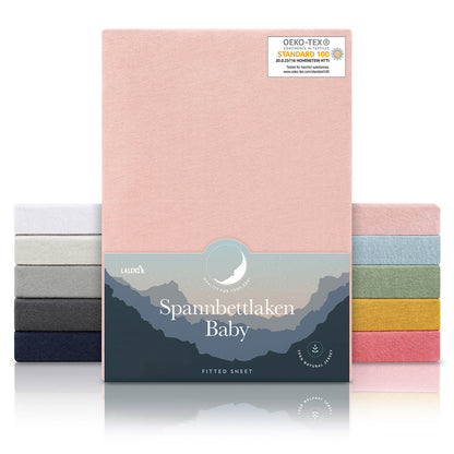 Verpackung von rosefarbenen Spannbettlaken für Babys mit Öko-Tex Standard 100 Siegel präsentiert neben einem Stapel Laken in verschiedenen Farben.