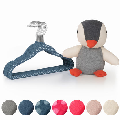 Stofftier Pinguin neben einem Stapel dunkelblauer Kinderkleiderbügel und Stoffmustern in verschiedenen Farben.