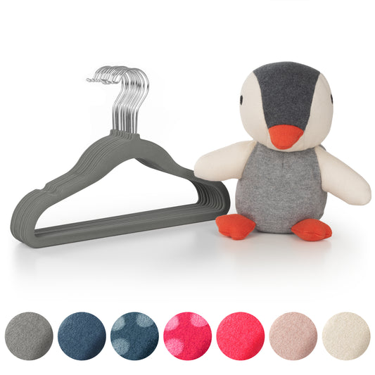 Stofftier Pinguin neben einem Stapel grauer Kinderkleiderbügel und Stoffmustern in verschiedenen Farben