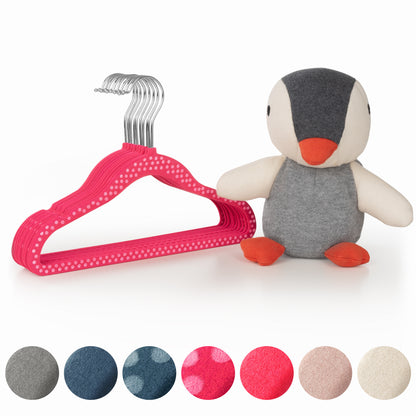 Stofftier Pinguin neben einem Stapel pinker Kinderkleiderbügel und Stoffmustern in verschiedenen Farben