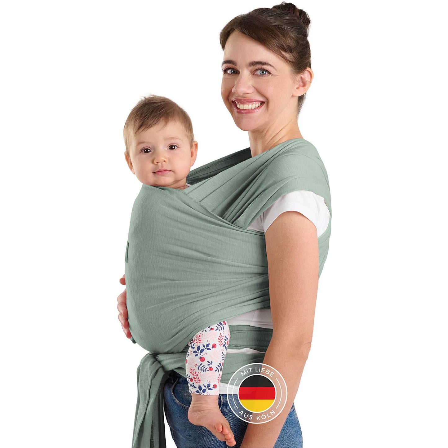 Frau mit Hochsteckfrisur trägt Baby in grüner Tragehilfe vor sich beide schauen zur Kamera.