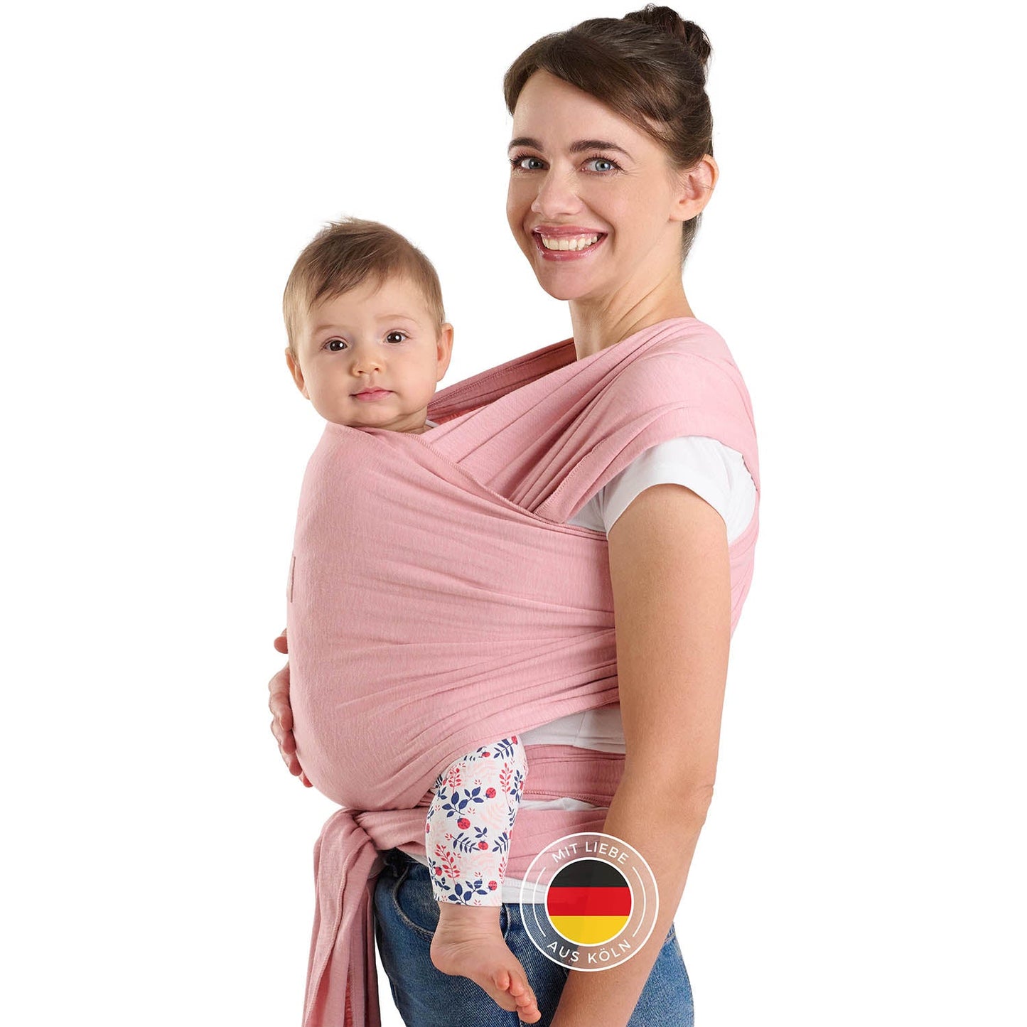 Frau mit Hochsteckfrisur trägt Baby in rosa Tragehilfe vor sich beide schauen zur Kamera.